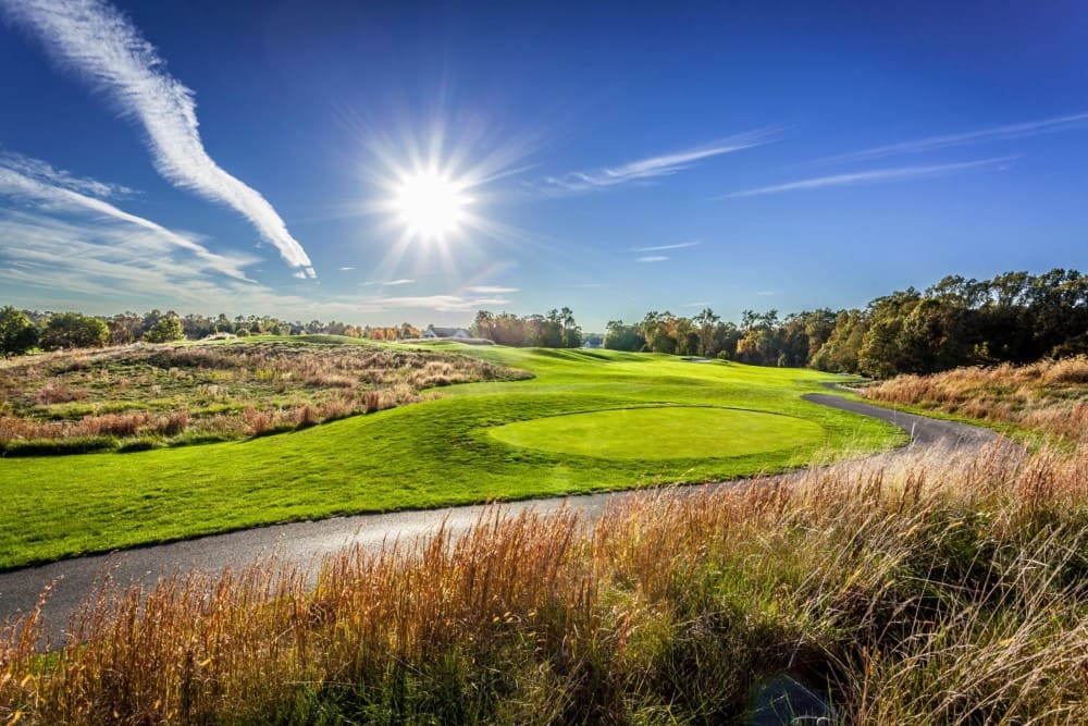Sun shining bright on a tee box and cart path with rolling fairway in the background.
