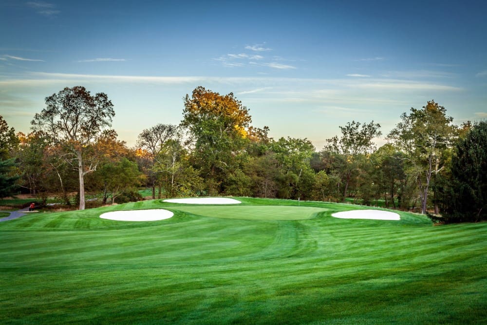 Well-manicured fairway leading to a green with woods in the background.