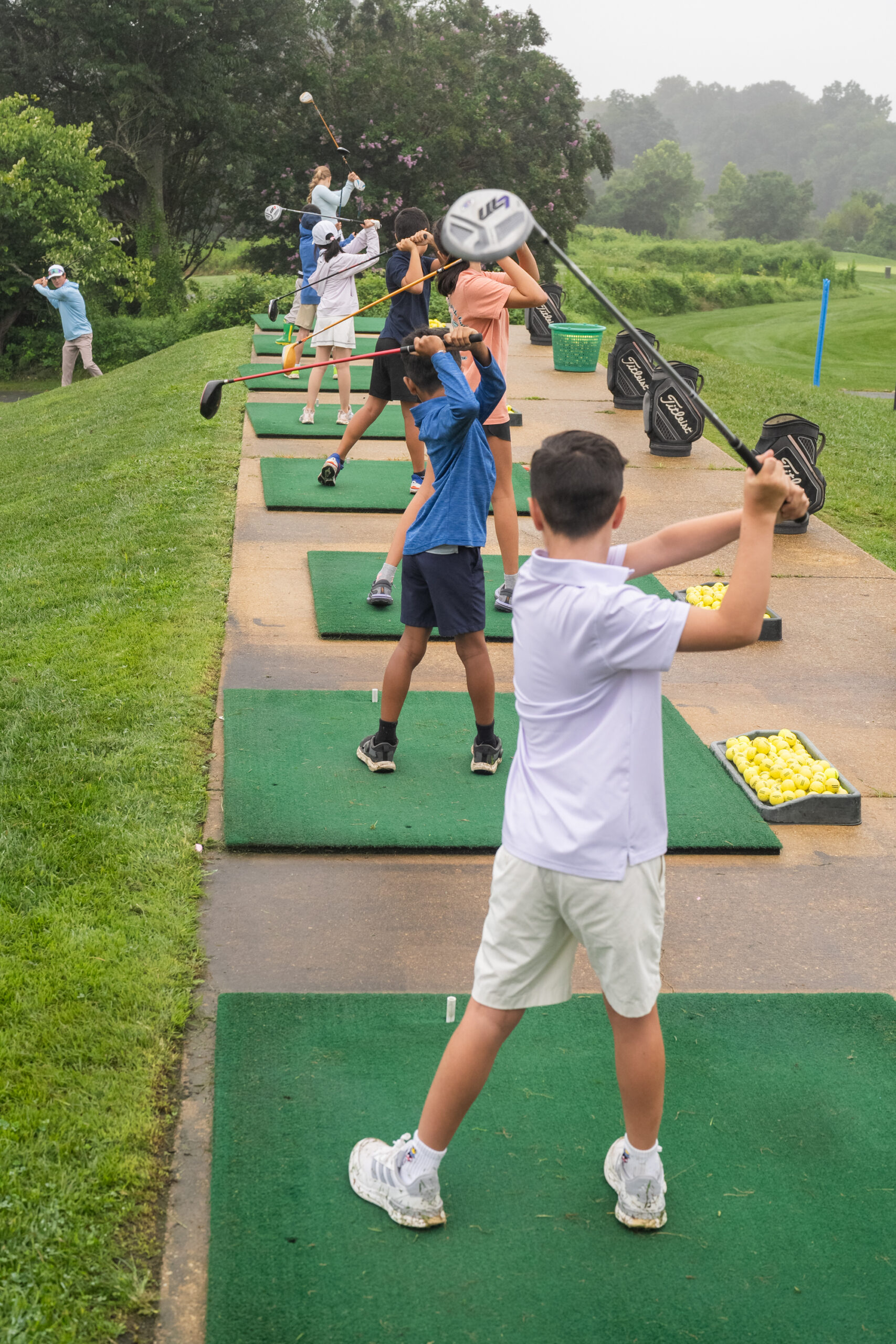 Kids swinging golf clubs on a driving range.