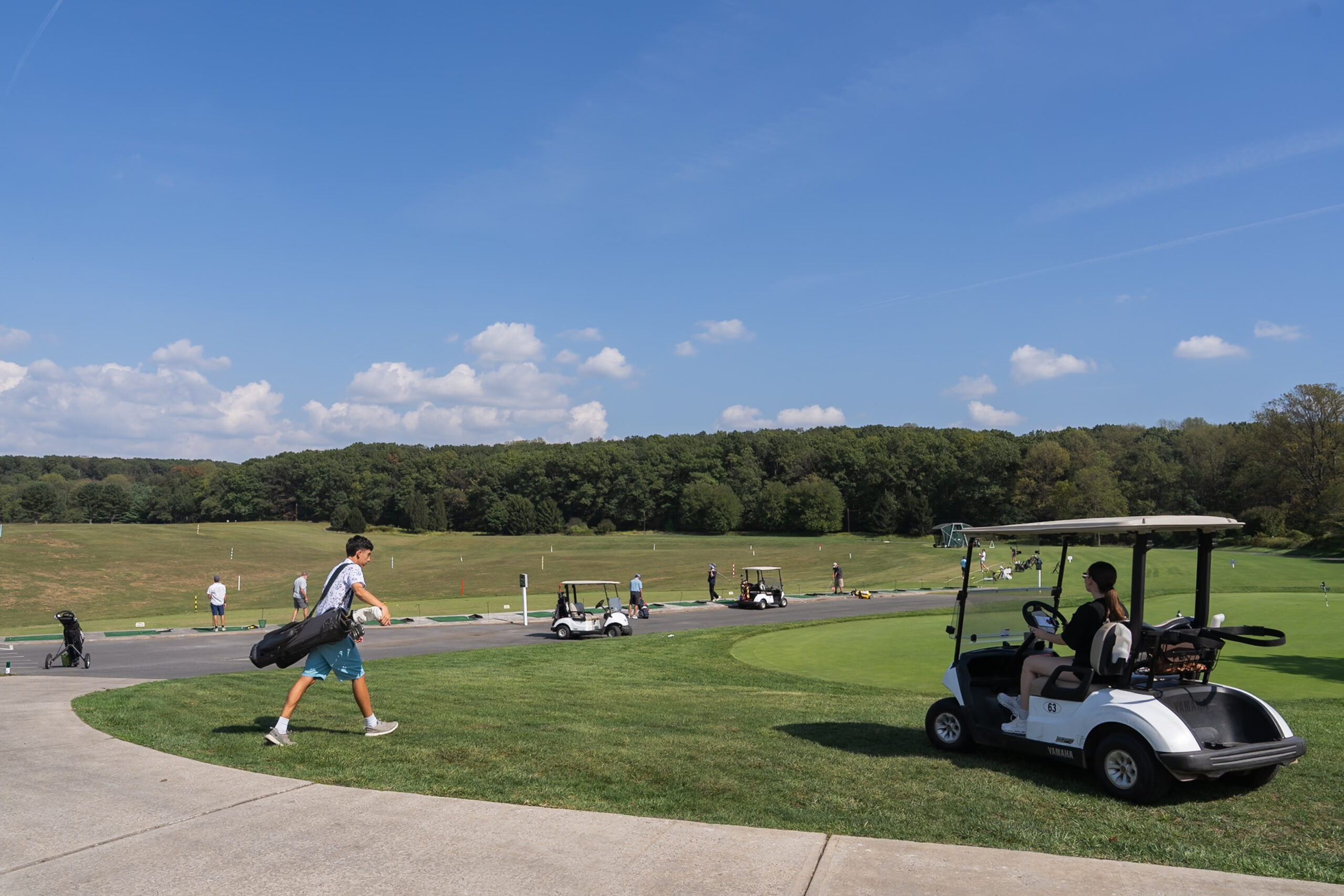 A golf course and driving range, with multiple golf carts and people.