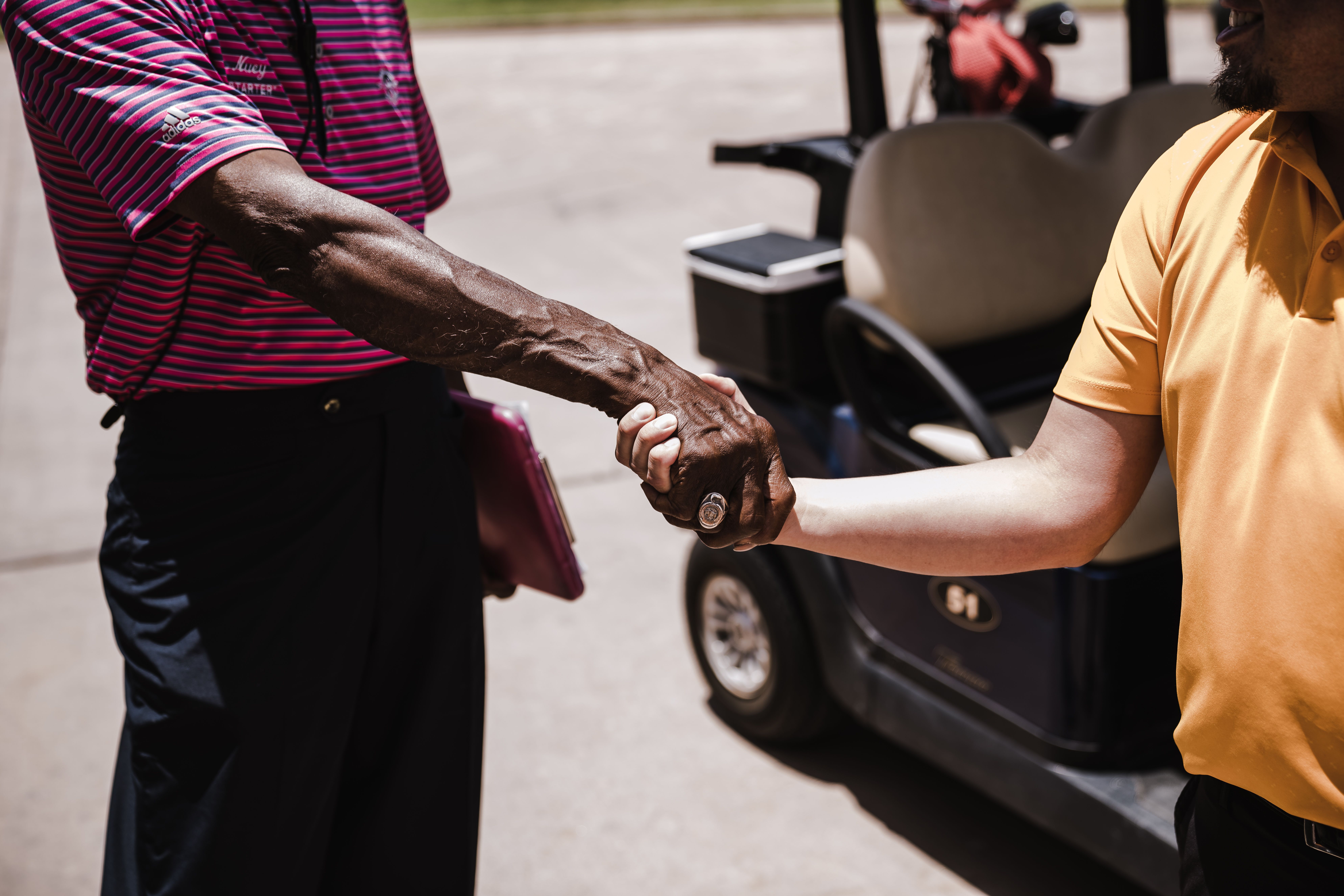 Two men shaking hands with a golf cart in the background.