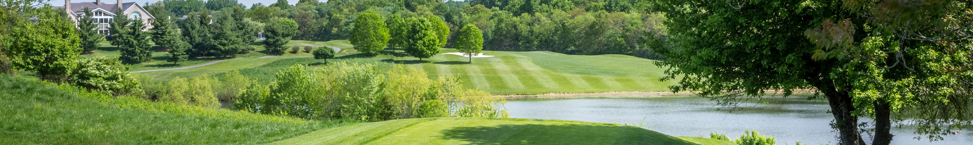 Lush green golf course with trees and a pond under a clear sky at Rattlewood Golf Course.